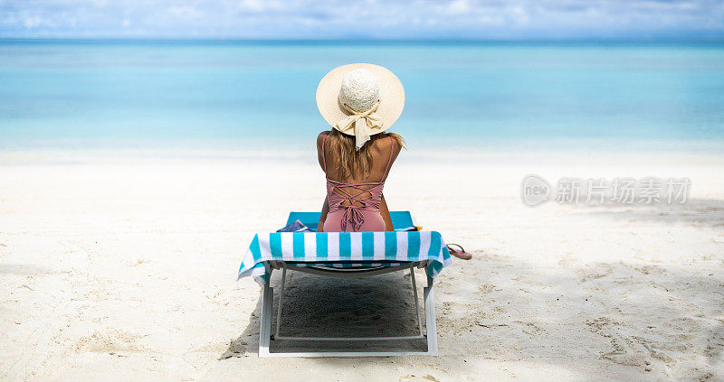 一个女人放松在沙滩上的躺椅上的全景。
