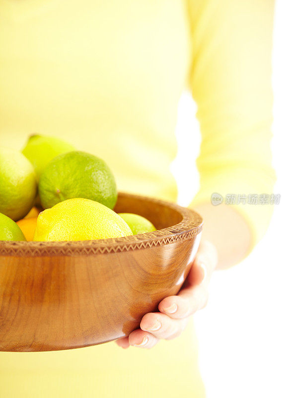 一个女人端着一木碗酸橙和柠檬