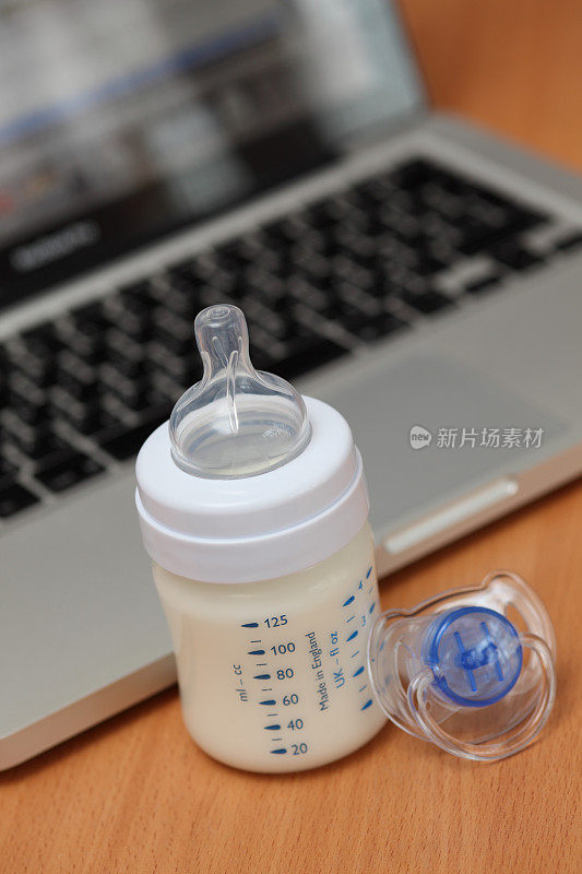 奶瓶、牛奶和奶嘴对着笔记本电脑