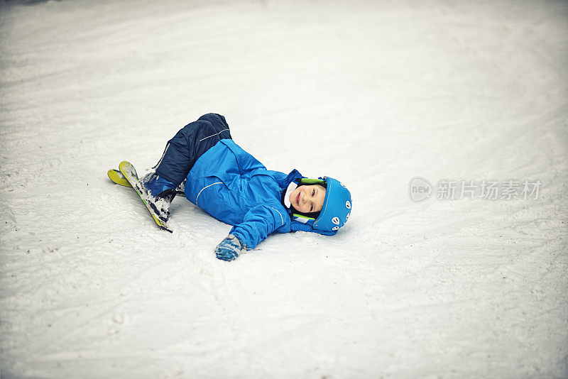 一个笑着的小男孩在上课摔坏后躺在雪地上