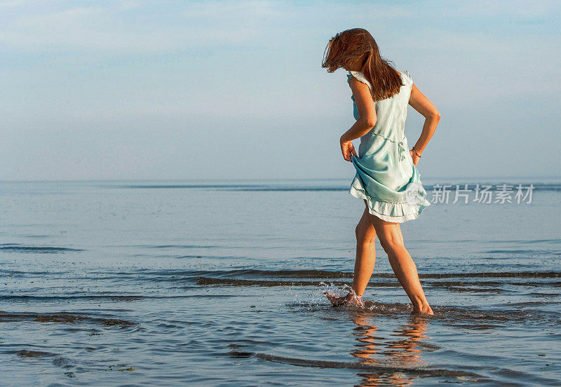一个年轻女子赤脚走在海滩的水里