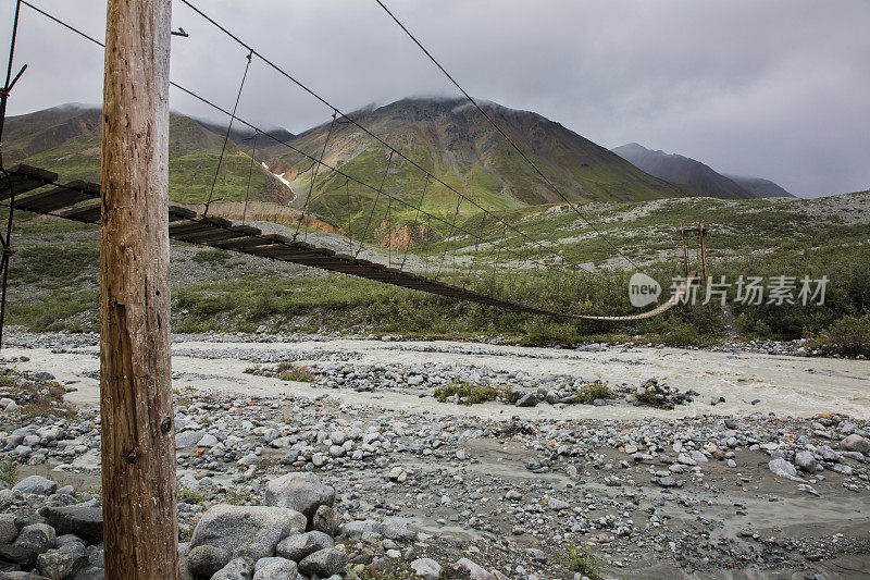 木制悬索桥横跨一条流淌的河流在阿尔