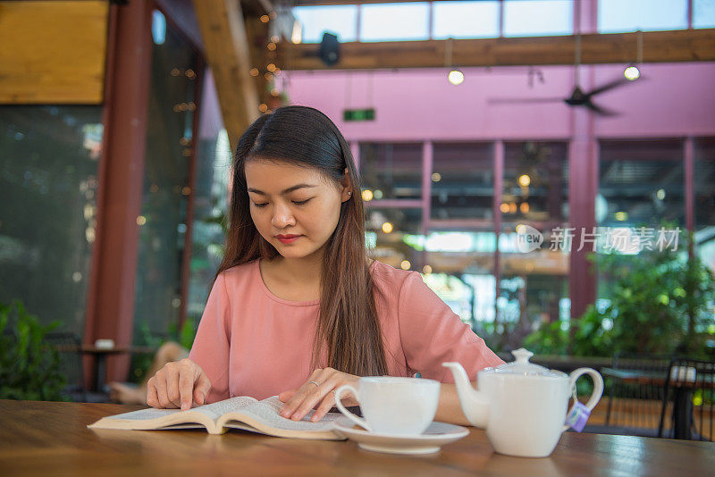 亚洲妇女享受她的周末与最喜欢的书籍和热茶