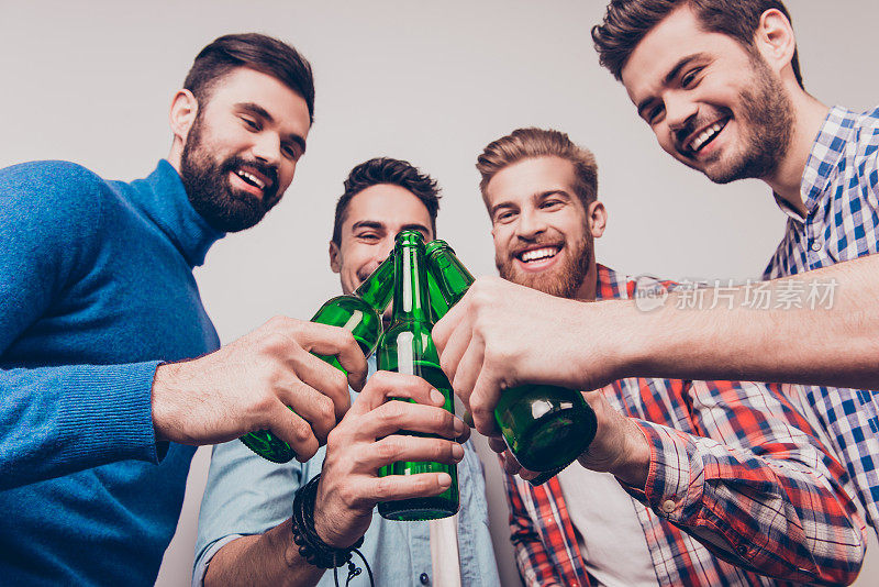 欢呼的男人!单身男人的生活。低角度照片四个快乐的朋友，碰杯啤酒。他们是体育比赛的球迷，如足球，篮球，曲棍球，棒球