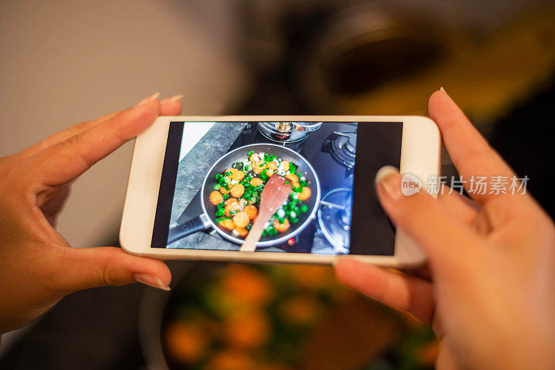 一个女人在厨房用智能手机拍摄健康饮食