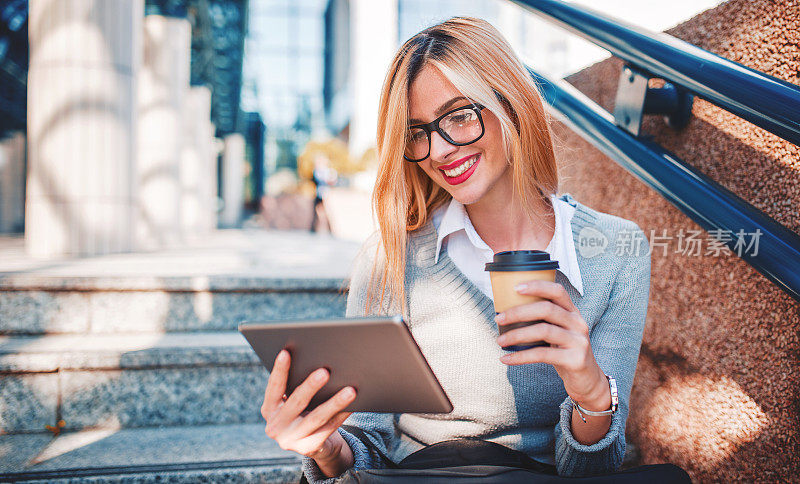 年轻的商业女性喝着咖啡，在户外使用数码平板电脑。商业、教育、生活理念