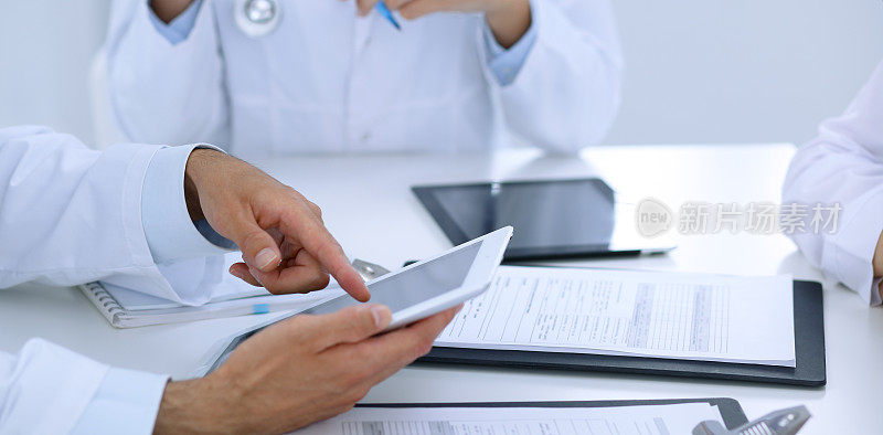 一群医生在开医学会议。医生使用触摸板或平板电脑的特写。