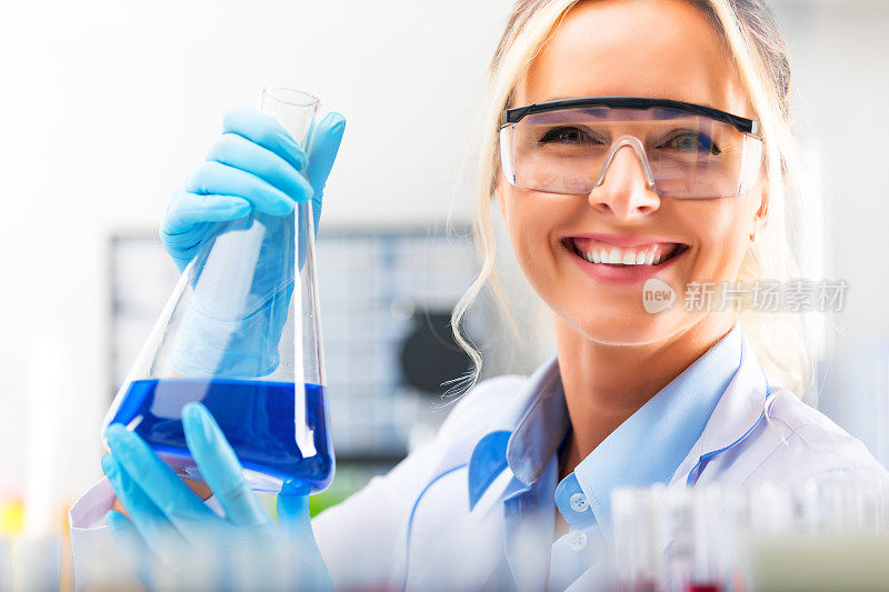 年轻迷人的女科学家在实验室里拿着一个装有蓝色液体物质的烧瓶