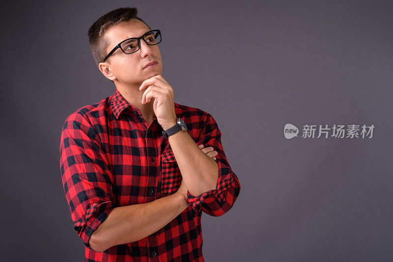 年轻英俊的男子穿着红色格子衬衫和眼镜在灰色的背景