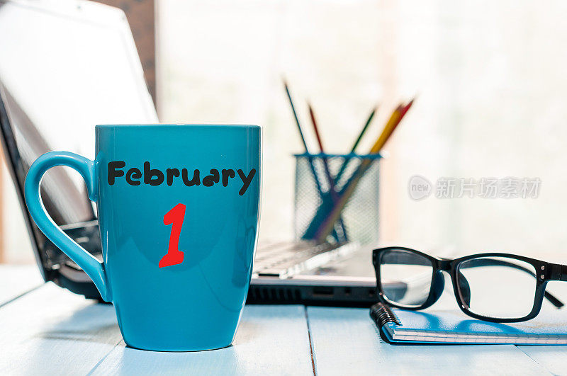 2月1日。月的第一天，日历上的早茶或咖啡杯在工作场所的背景。