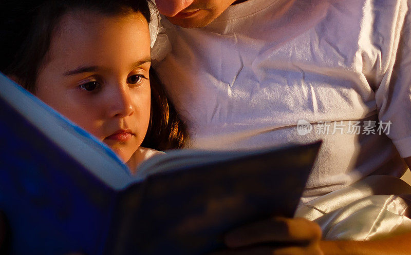 一位慈爱的父亲在给他的小女儿读睡前书