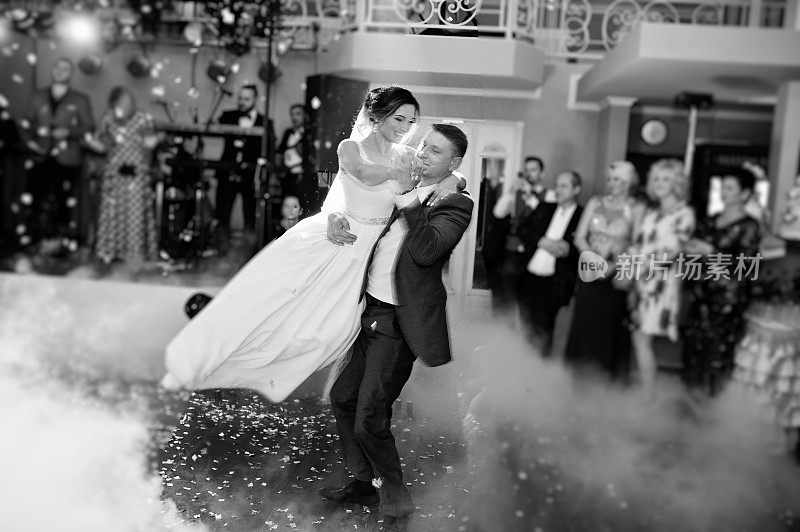 新婚夫妇在他们的婚礼上以浓重的烟雾和彩灯为背景跳舞。黑白照片。