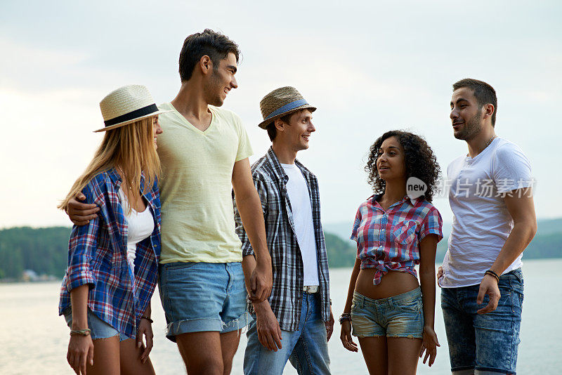 愉快的年轻朋友们穿着休闲服装沿着海岸散步，讨论假期计划