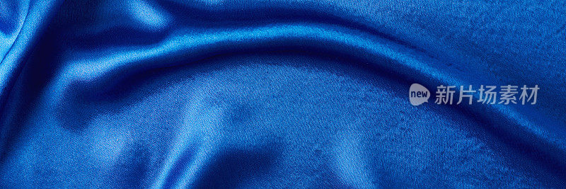 有褶皱的蓝色丝绸背景。抽象纹理的波纹缎面，长横幅
