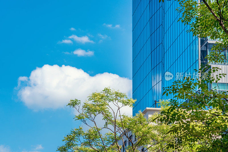 在日本东京，仰望现代城市天际线的全景，蓝天绿树