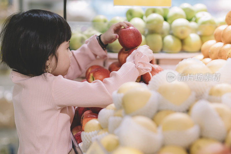 一个亚洲的中国女孩在超市的水果店捡红苹果