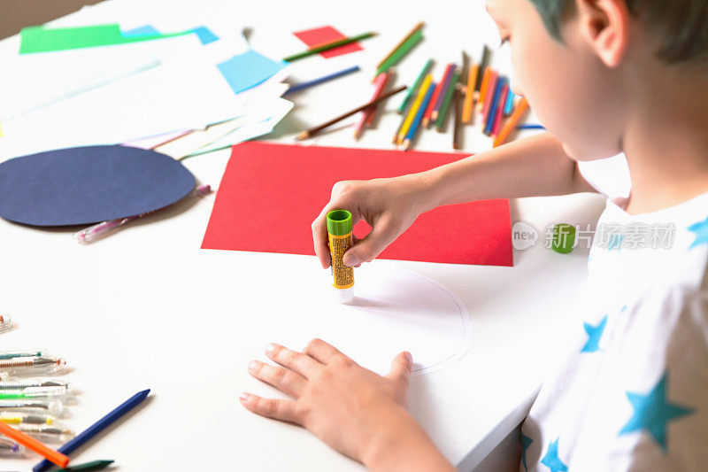 男孩用颜色、纸张和胶水手工制作卡片。孩子们艺术和手工艺。