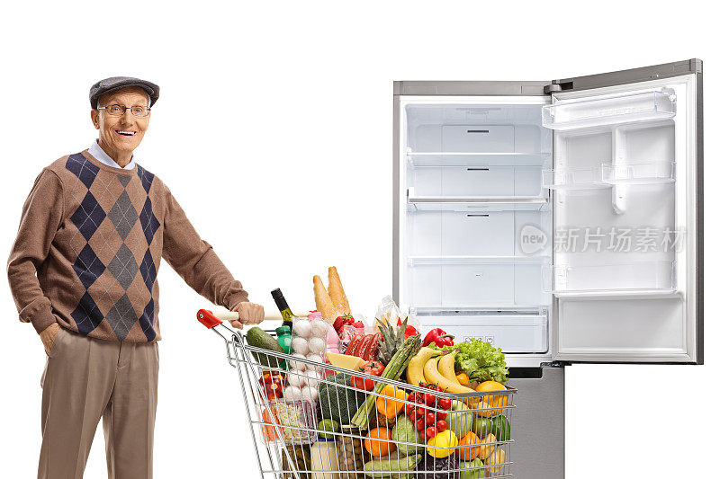 一个老人推着装满食物的购物车站在一个空冰箱前