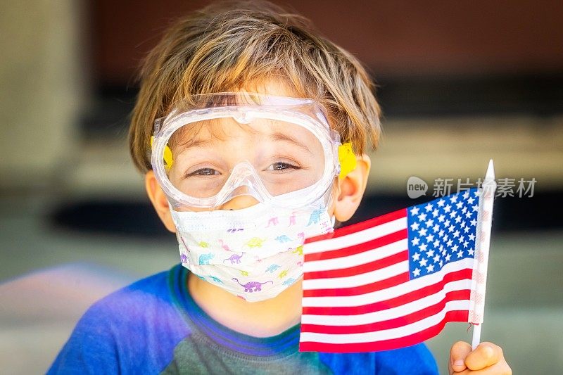 小男孩戴着防护面具和眼镜，举着一面小美国国旗