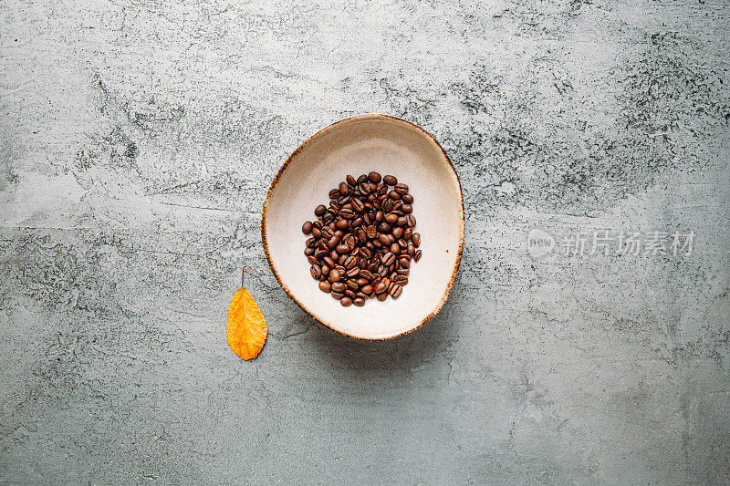 秋天的概念与咖啡豆和黄叶在混凝土背景与复制空间