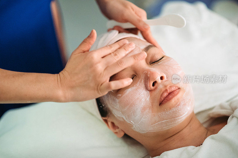亚洲华人女性美容师，在美容院给一位女士敷面膜