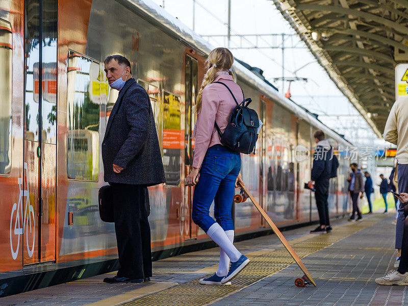 一个戴着防护面具的金发少女站在火车前面的站台上。