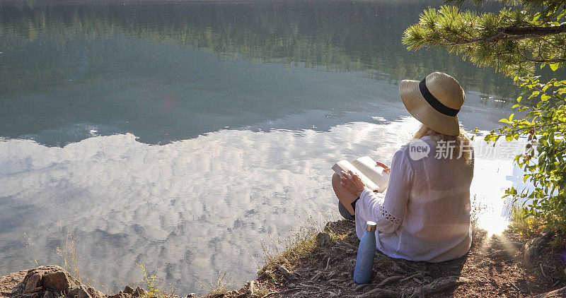 成熟的女人在湖边放松，带着书