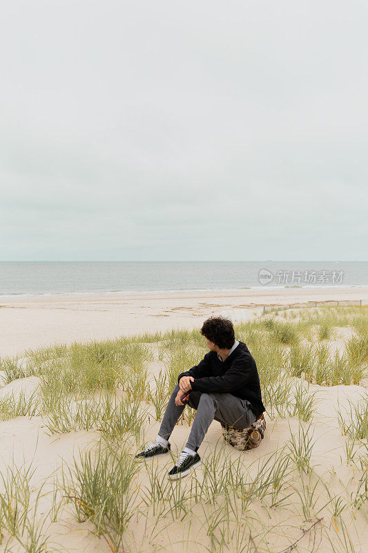 年轻男子坐在海滩附近的沙丘上