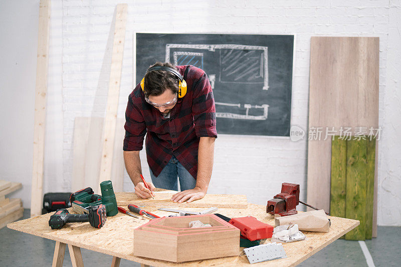 在木工车间，手拿铅笔，辛勤工作的专业木匠分析项目。背景里有一张钳工桌和一些工具