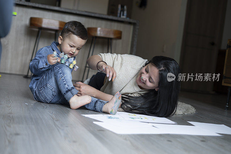 一位单身母亲和她1到2岁的孩子在客厅里玩耍的美丽时刻，她的房子的地板上放着画