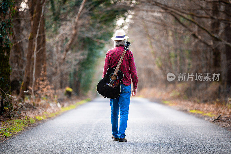 一个背着吉他走在乡间小路上的自由流浪汉