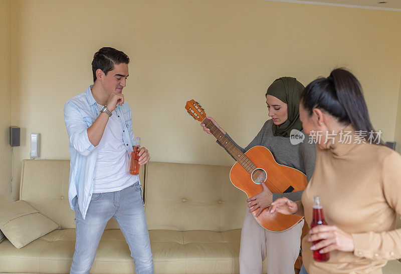 一群年轻的多元文化朋友在一起度过美好的时光，享受着穆斯林妇女演奏的吉他声。