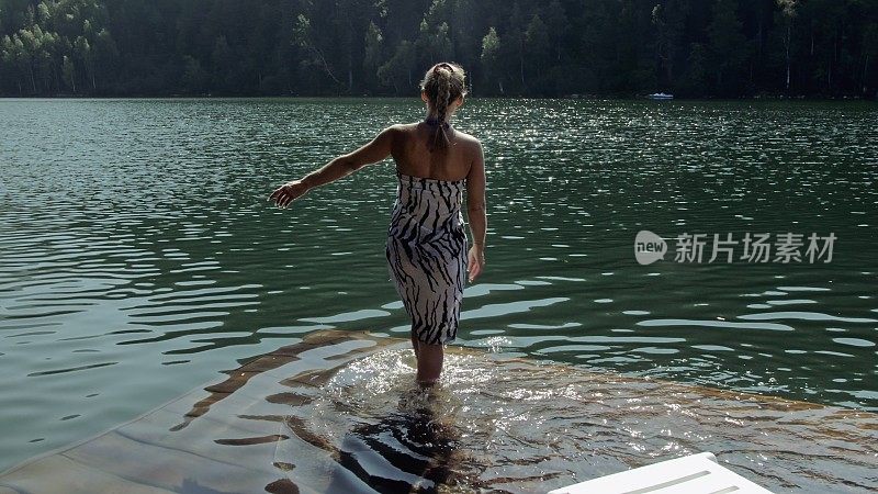 一个女人戴着太阳镜，披着波西米亚丝绸披肩，躺在日光浴床上。女孩在洪水木水下码头上休息。湖面上铺满了水。