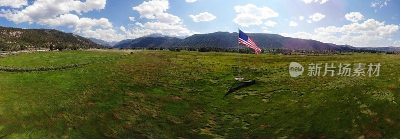 美国国旗在科罗拉多州西南部靠近特柳赖德和乌雷的岩石山脉的草地上飘扬，这是一个晴朗的多云的日子，云层美丽