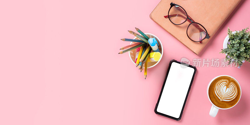 办公桌与空白屏幕智能手机，笔，笔记本，眼镜，咖啡杯在粉红色的背景