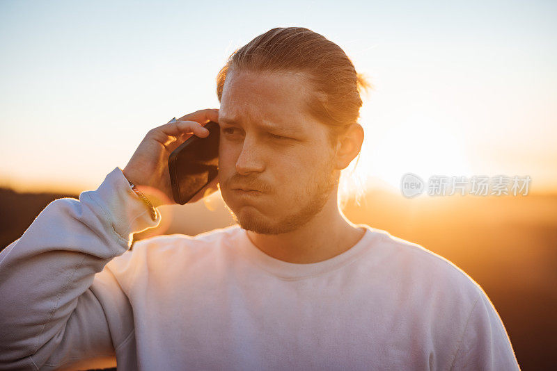 坏消息:一名年轻人在夕阳下用手机户外活动