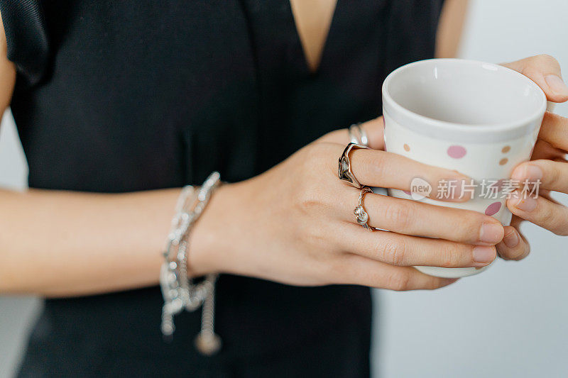 这是一个女人拿着一杯咖啡，用白色的背景装饰着钻石戒指和银手镯等奢侈品