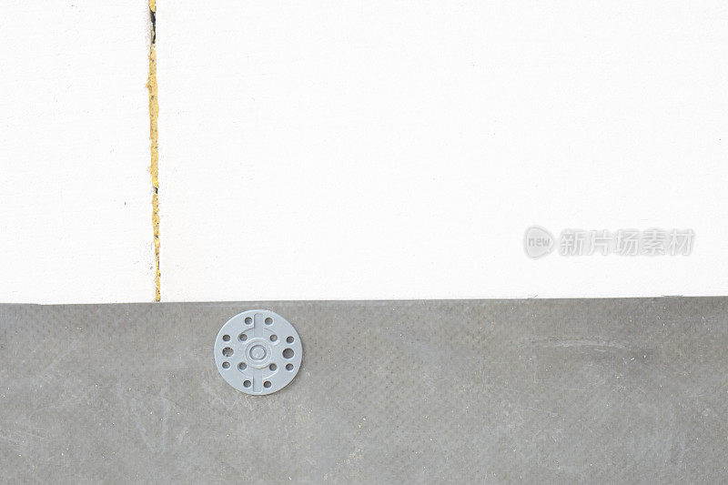 灰色塑料钉头将橡胶类屋面材料附着在泡沫混凝土砌块砖墙上。