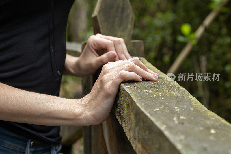 一个人的手放在粗糙的木制扶手上，指节、手腕和手指