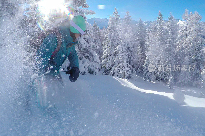 镜头耀斑:年轻女子在树上滑雪时向相机喷洒粉末雪。