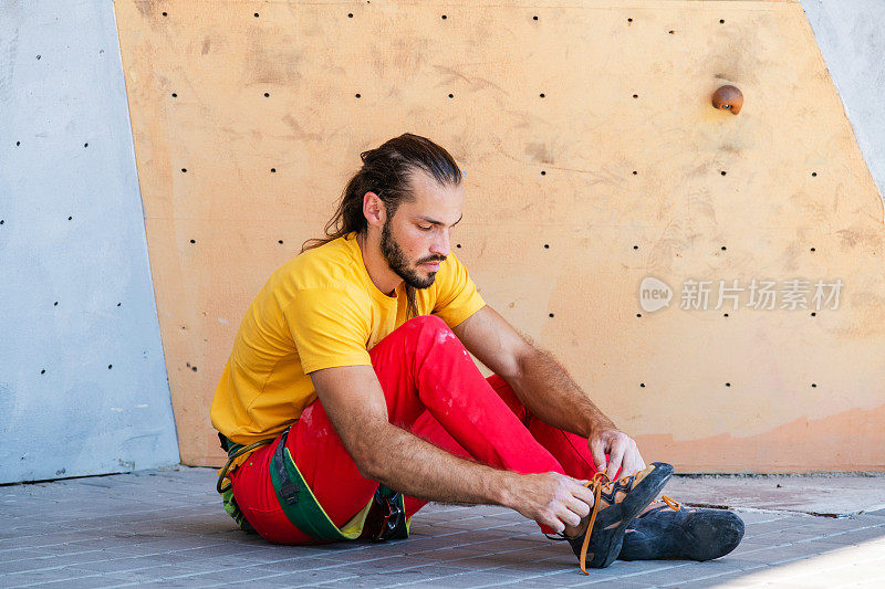 一名男子坐在攀岩墙前，穿上了攀岩鞋。