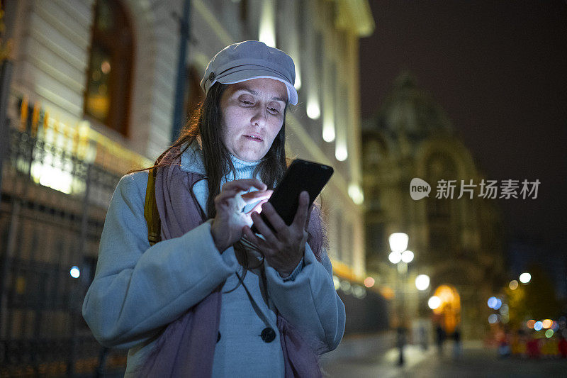 一个晚上在城里拿着手机的女人。城市打破。