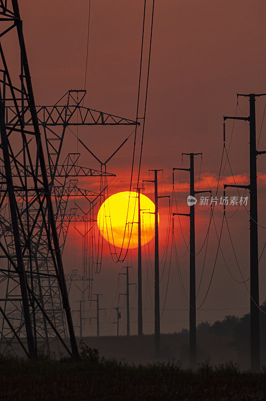 炎炎夏日，太阳落在一排高压输电塔和电线杆后面