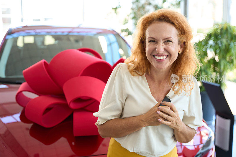 快乐的女人站在新车旁边，手里拿着钥匙