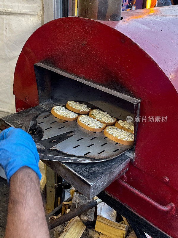 不可识别的人穿着蓝色，橡胶手套滑迷你披萨到户外，不锈钢，石基础披萨烤箱上长柄披萨桨，关注前景