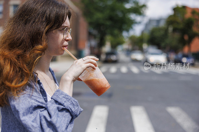 忙碌的年轻女子喝着橘子冰沙，过马路在布鲁克林，纽约