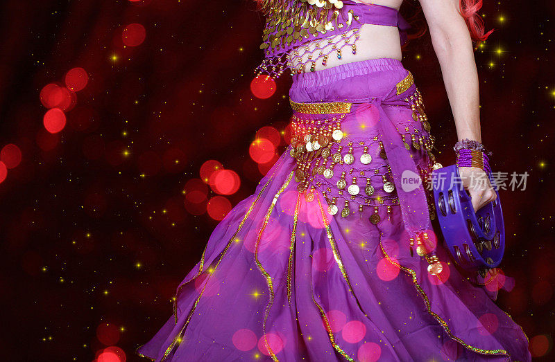 特写肚皮舞者穿着紫色的舞蹈服装与彩色散景灯