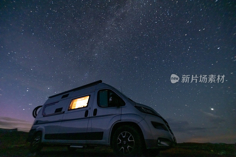 一辆露营车从里面被照亮，站在一个高原上，夜晚繁星点点，没有月亮。