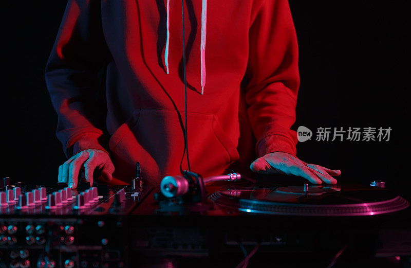 穿着红色连帽衫的年轻DJ在夜总会的唱盘上刮黑胶唱片。在舞台上播放音乐的嘻哈音乐节目主持人的手