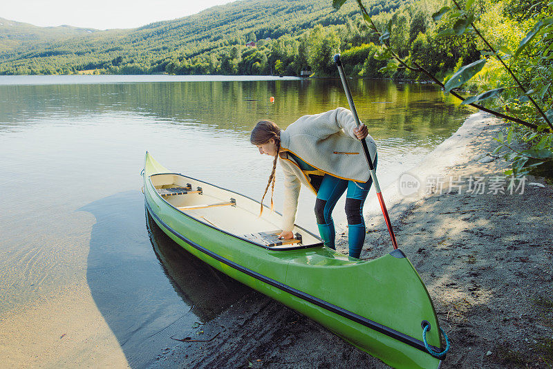 在挪威风景优美的湖上，一名梳着辫子的女子正准备乘独木舟航行